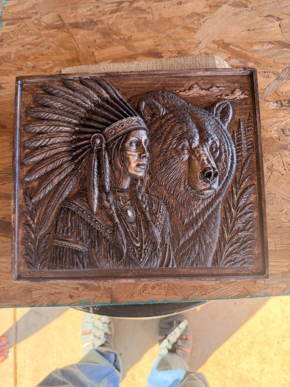 Finished relief of an Indian woman wearing a feathered headdress beside a bear, with a dark glaze highlighting the carved details